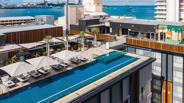 Ein Pool auf dem Dach mit Liegestühlen und Sonnenschirmen, mit Blick auf eine Küstenstadt.