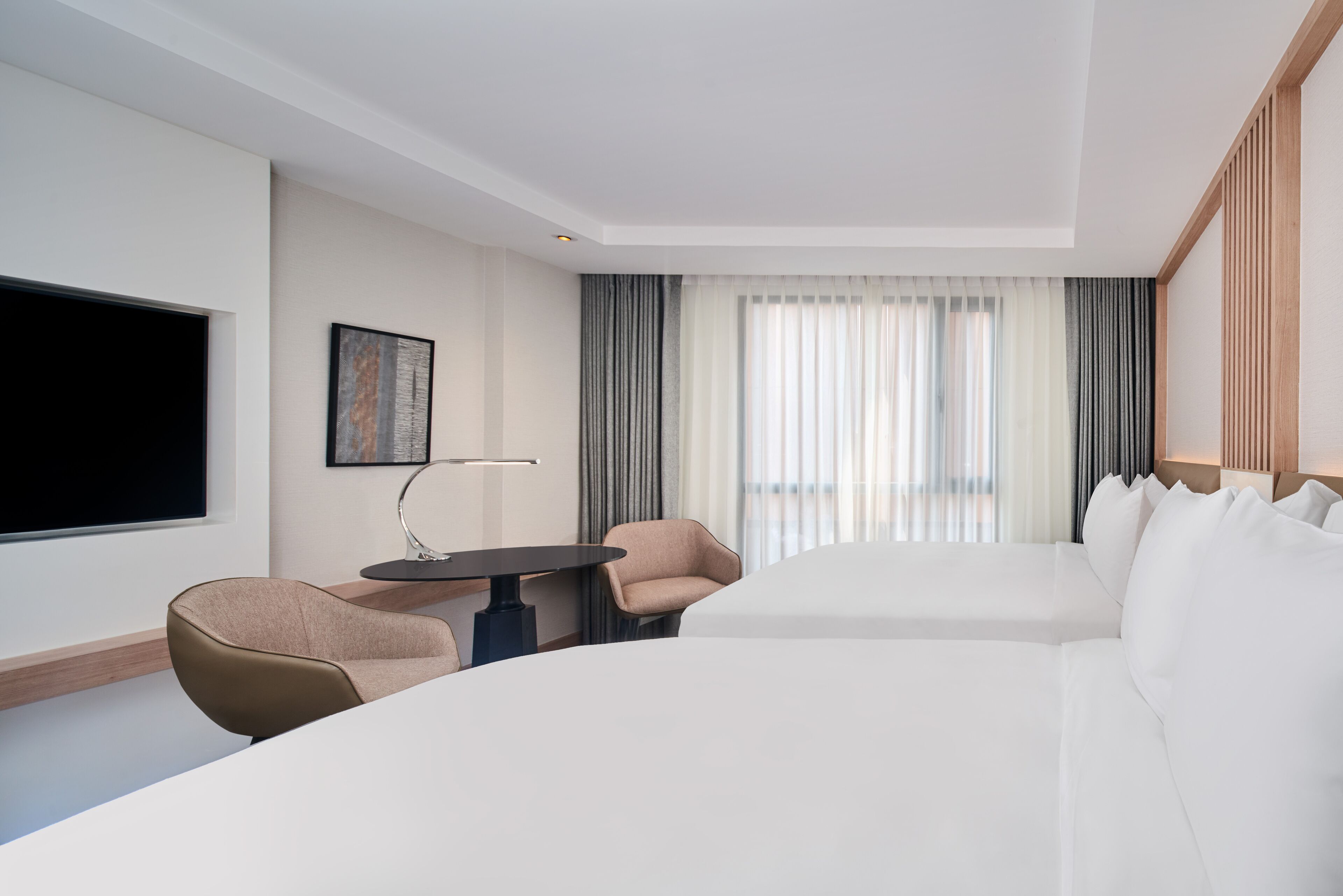 A modern hotel room with a large bed, a desk, a chair, and a TV.