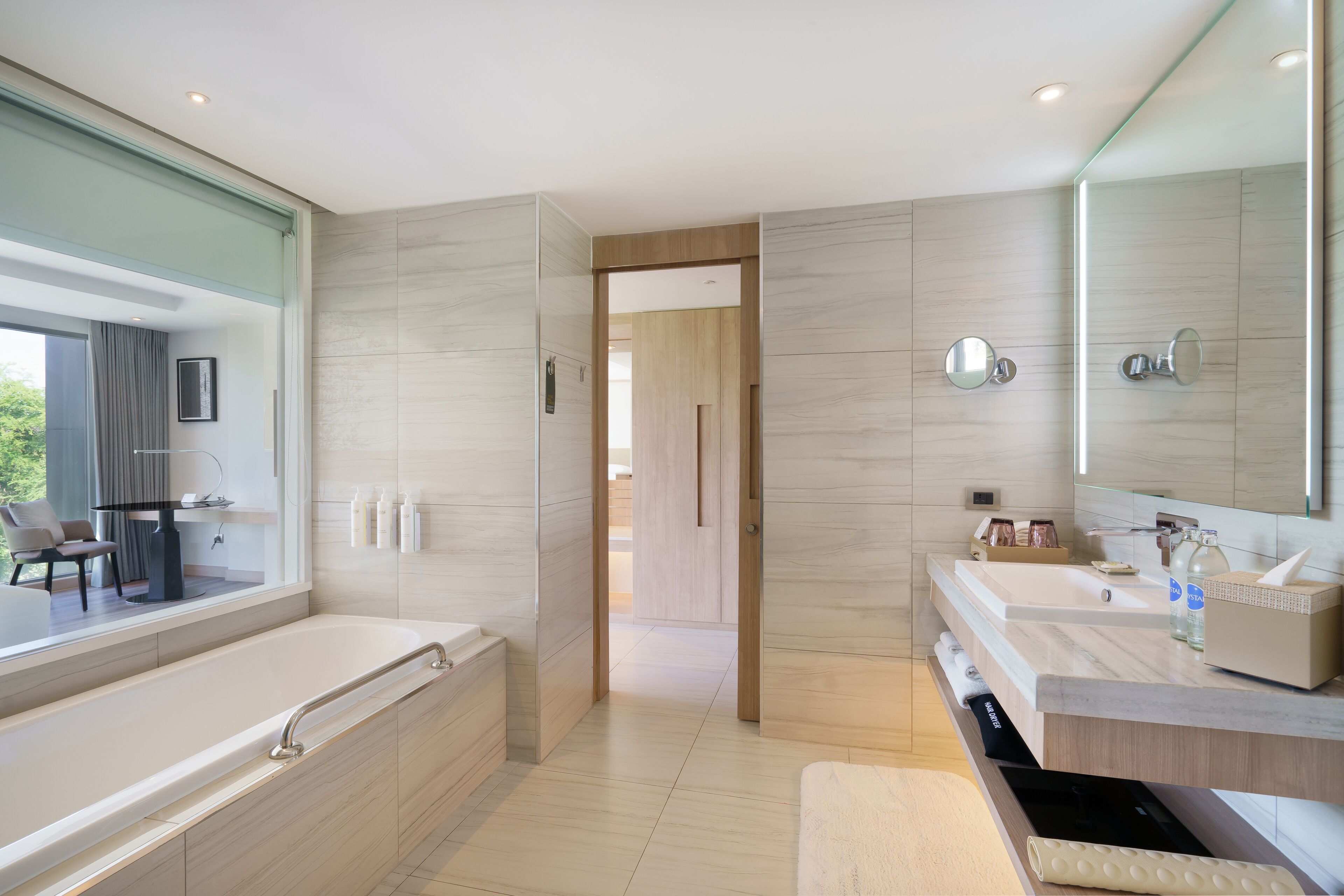 A modern bathroom with a large bathtub, two sinks, a mirror, and a view of a balcony.