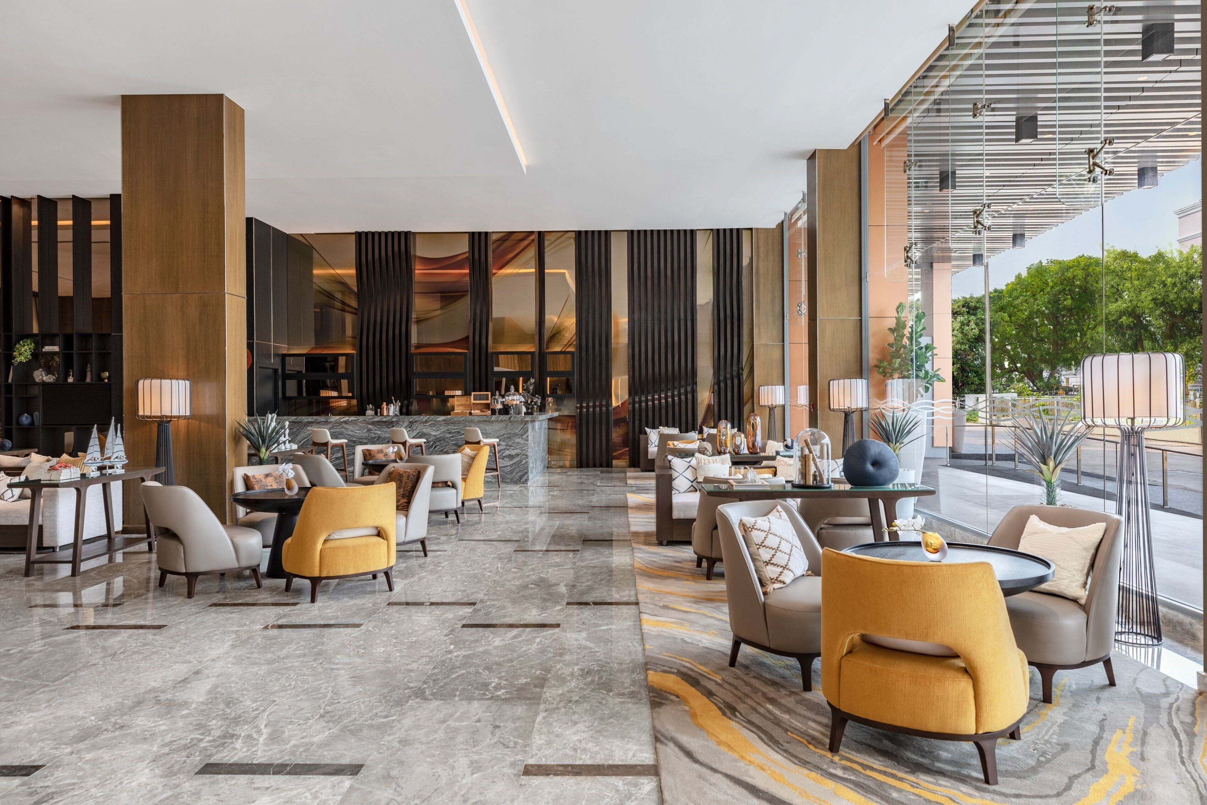 Un moderno vestíbulo de hotel con suelo de mármol, mobiliario contemporáneo y amplios ventanales con vistas al exterior.