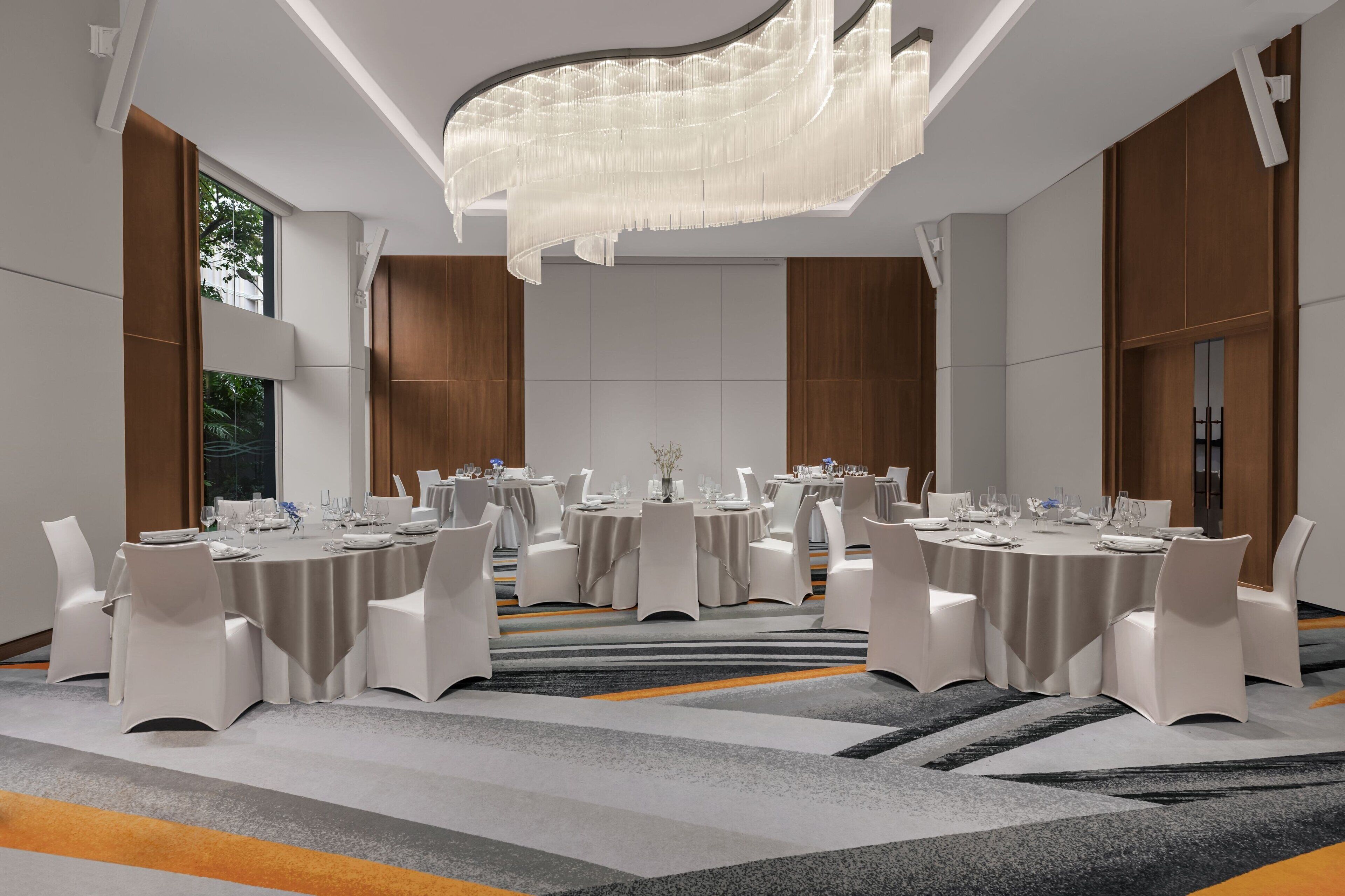 A modern conference room with multiple round tables, white chairs, and a large chandelier.