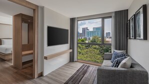 Ein modernes Wohnzimmer mit großem Fenster, einem Flachbildfernseher, einem grauen Sofa und einer Holzvertäfelung.
