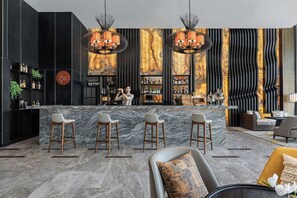 A modern bar area with marble countertops, bar stools, and a bartender.