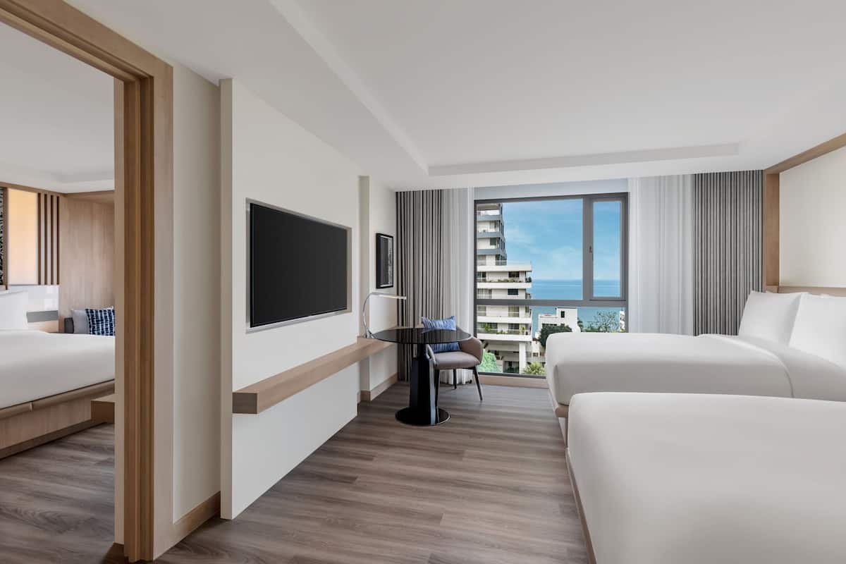 Une chambre d’hôtel avec deux lits, une télévision, un bureau et un balcon offrant une vue sur la ville.