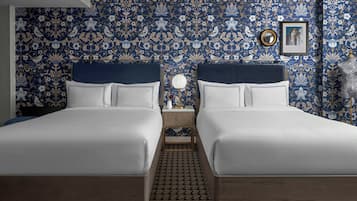 A double bed room with a patterned wallpaper, a bedside table with a lamp, and a framed picture on the wall.