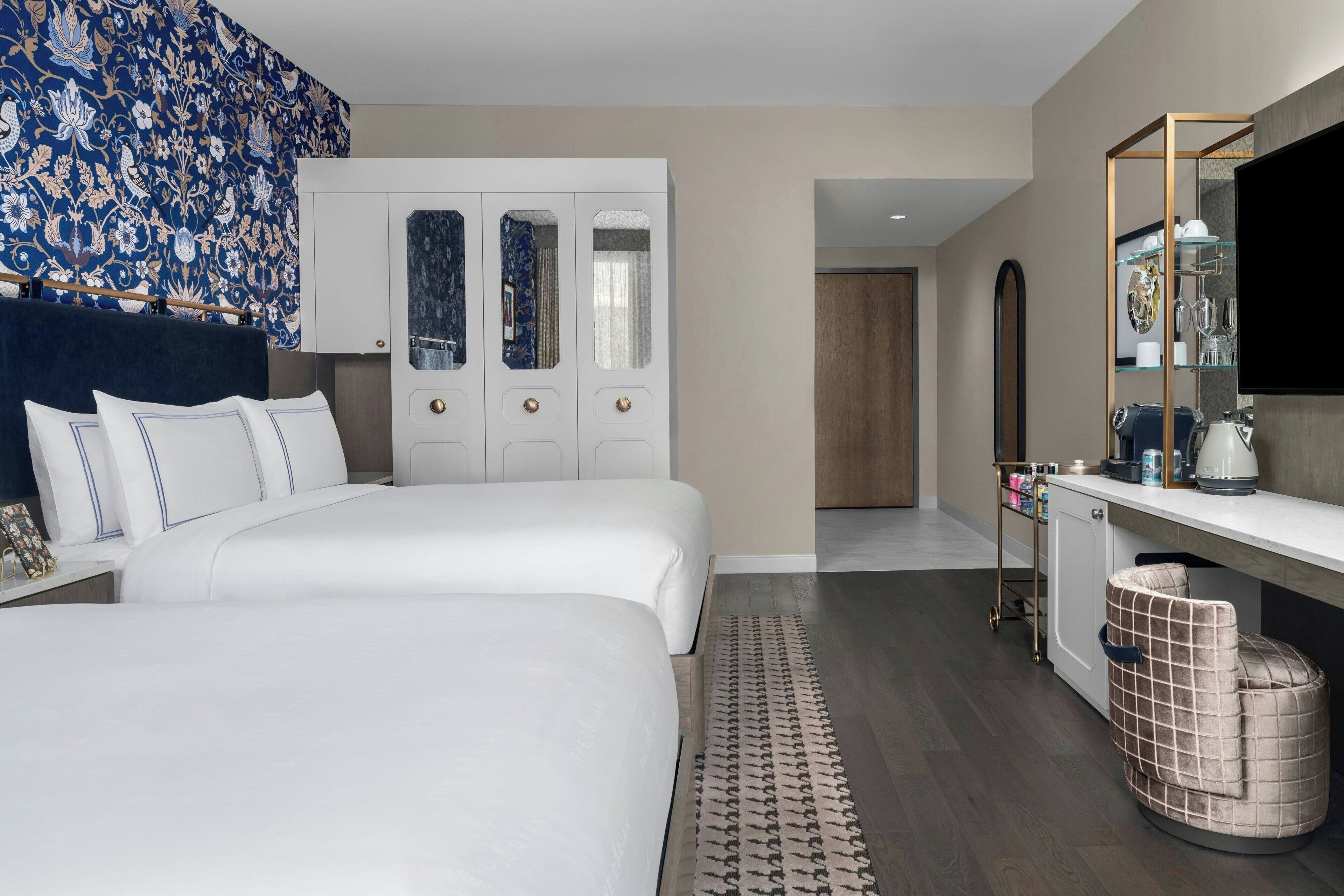 A modern hotel room with a large bed, a desk with a mirror, a wardrobe, and a television.