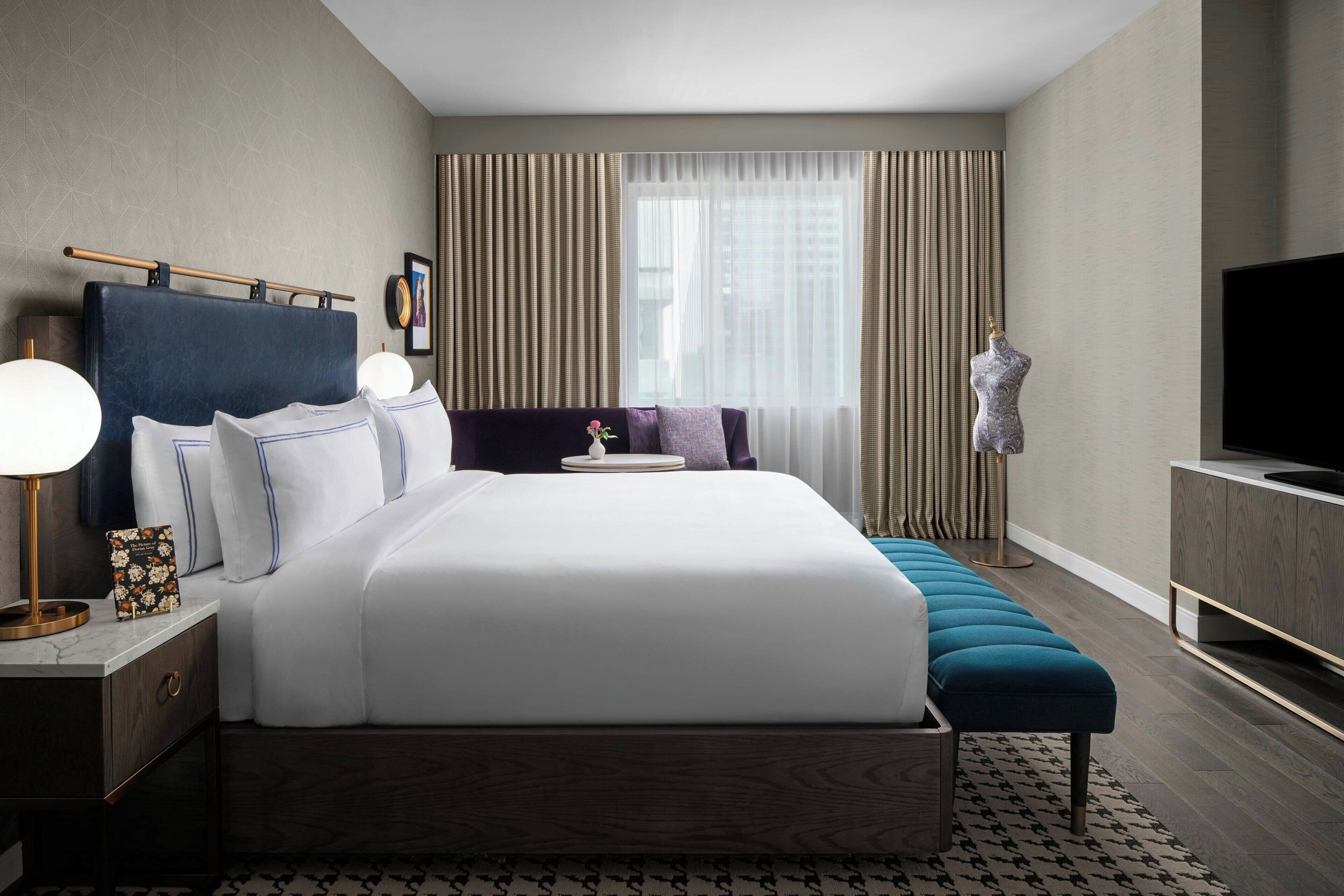A modern hotel room with a large bed, bedside tables, a TV, and a bench.