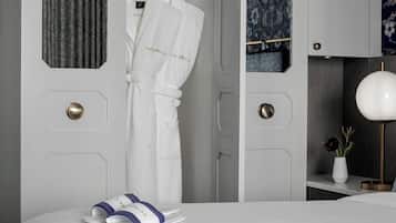 Una habitación de hotel con cama, bata, pantuflas, un jarrón con flores y una lámpara.