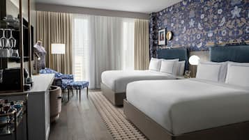 Habitación de hotel con dos camas, un escritorio con silla, una tocador con espejo y un papel tapiz estampado.