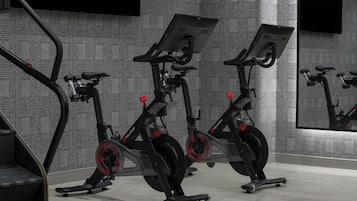 Three stationary bikes in a room with a textured gray wall and a large mirror reflecting the bikes.