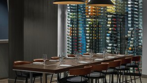 A dining area with a long table set for six, surrounded by chairs, and a wine rack with numerous bottles in the background. - The Dorian, Autograph Collection (Calgary)