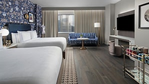 A hotel room with two beds, a sofa, a TV, and a minibar. - The Dorian, Autograph Collection (Calgary)