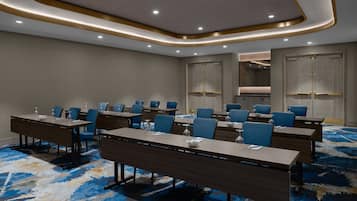 A conference room with long tables, blue chairs, and a patterned carpet.