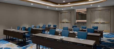 Un salón de conferencias con largas mesas, sillas azules y una alfombra estampada.
