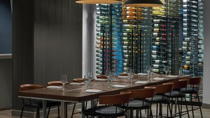 Een moderne eetruimte met een lange tafel, meerdere stoelen en een wijnrek op de achtergrond.