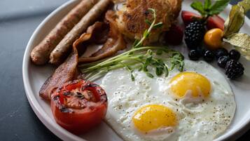 A breakfast plate with eggs, bacon, sausages, tomatoes, and berries.