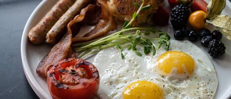 Un plato de desayuno con huevos, tocino, salchichas, tomates y frutos rojos.