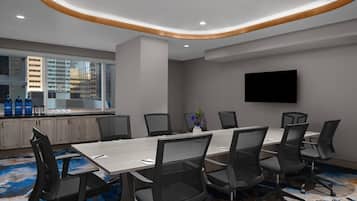 A conference room with a long table, multiple chairs, a flat-screen TV, and a city view through large windows.
