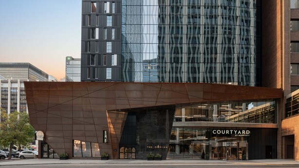 A modern building with a glass facade reflecting the sky. In front, there's a structure labeled "COURTYARD BY MARRIOTT" with a large entrance and a sign for "THE DORIAN."