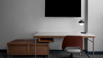 A modern office desk with a flat-screen monitor, a desk lamp, a red office chair, and a mobile cart with drawers.