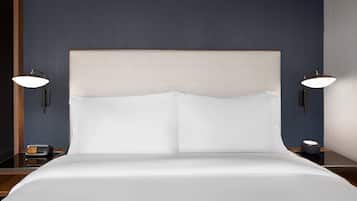 A neatly made bed with a headboard, two bedside lamps, and a small table with a clock and a cup.