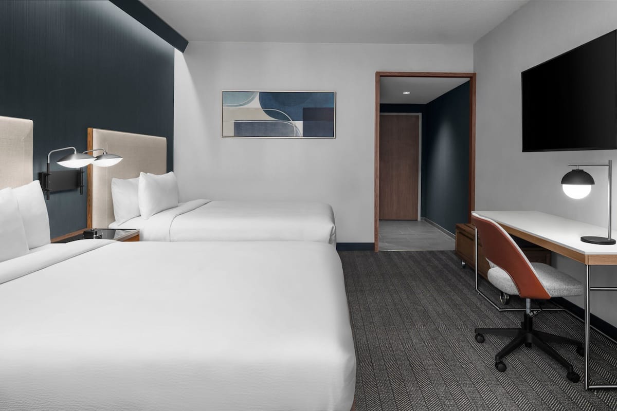 A hotel room with two beds, a desk, a chair, a TV, and a painting on the wall.