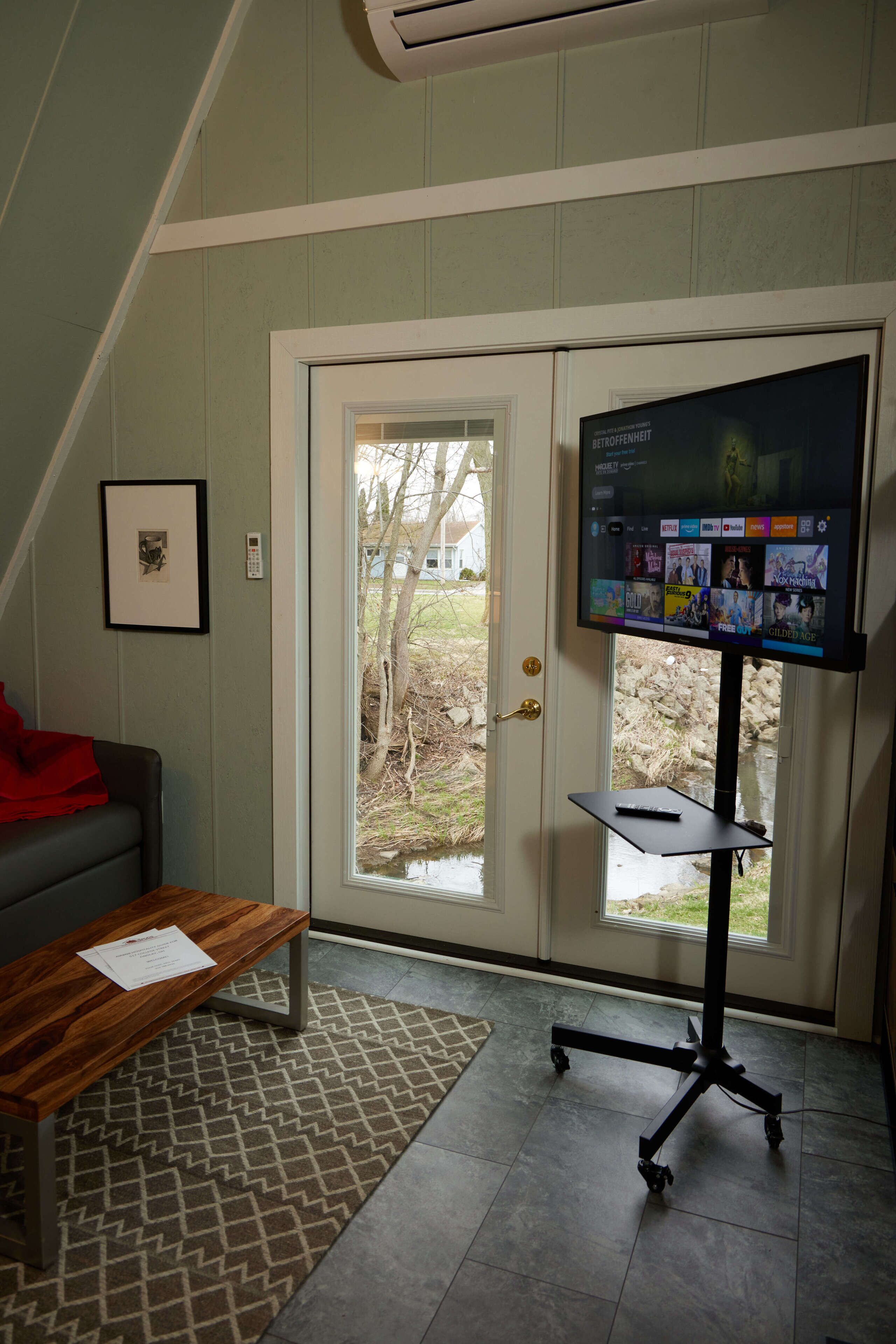A room with a television on a stand, a door leading outside, a small table with a document, and a framed picture on the wall.