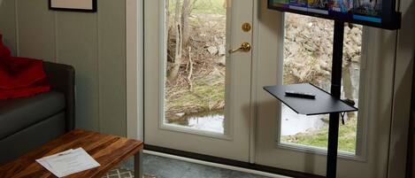 A room with a television on a stand, a door leading outside, a small table with a document, and a framed picture on the wall.