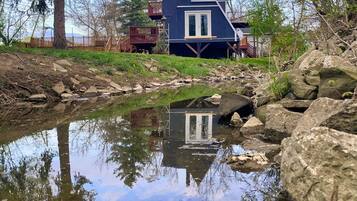 Situated lakeside, this house offers a serene escape with a raised platform, wooden deck, and staircase to an upper level.