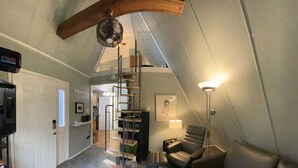 A modern loft bedroom with a spiral staircase, a sofa, a lamp, and a view of the living area.