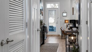 A hallway with white doors, a kitchen area, a dining table with chairs, and a coffee machine.