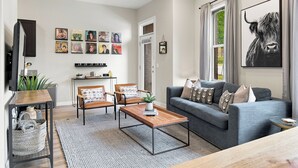 A modern living room with a grey sofa, two armchairs, a coffee table, and a TV mounted on the wall.