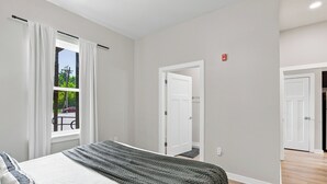 A bedroom with a bed, a window with curtains, a door, and a view of the outdoors.