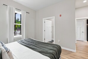 Un dormitorio con cama, ventana con cortinas, una puerta y vistas al exterior.