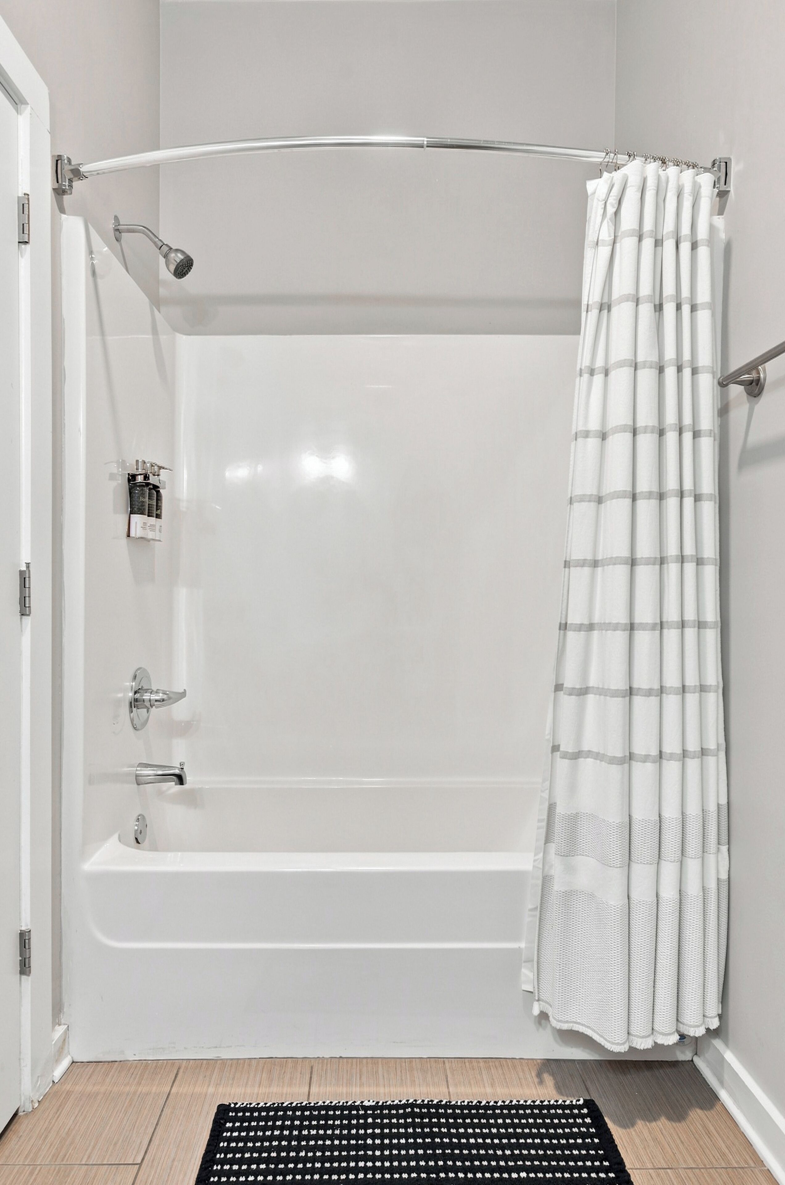A standard white bathtub with a shower head and faucet, a towel rack, and a striped shower curtain.