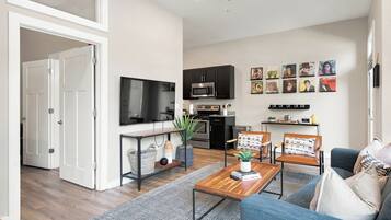 A modern living room with a sofa, coffee table, and TV. There is a kitchen area with cabinets and a microwave.
