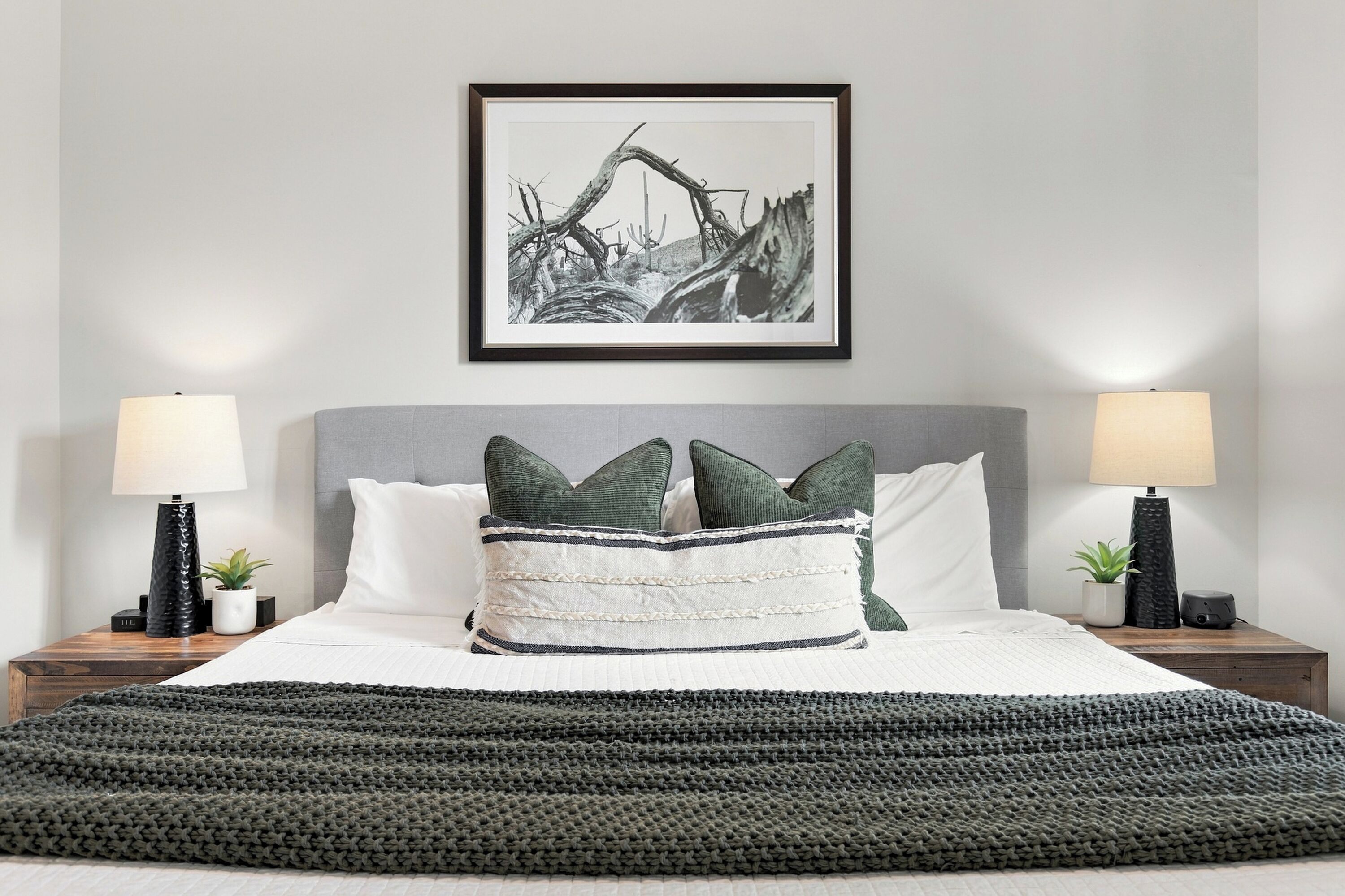 A neatly made bed with a grey knitted throw, two bedside lamps, and a framed black and white photograph on the wall.