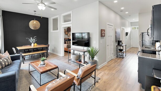 A modern living room with a dining area, a kitchen, and a hallway.