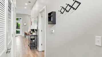 A hallway with a white door, a coat rack, a small table with a coffee maker, and a wall-mounted shelf.
