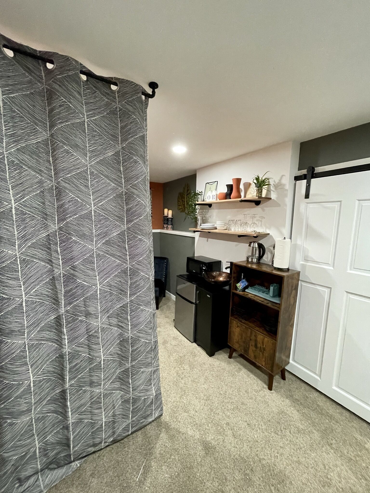 A compact kitchen with a refrigerator, microwave, and coffee maker. There are shelves with decorative items and a door with a black handle.