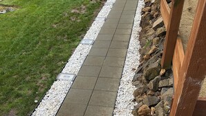 A pathway with alternating stone tiles and pebbles, bordered by a grassy area and a wooden structure. - Private getaway in a beautiful neighborhood (Salem)