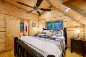 Ein Schlafzimmer einer Holzhütte mit einem Bett, einem Deckenventilator, einem Fenster und einer Tür.