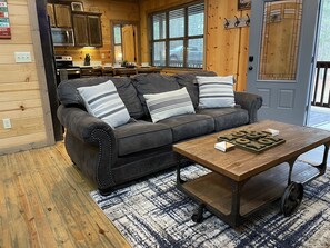 Ein gemütliches Blockhauss-Interieur mit einem dunkelbraunen Ledersofa, einem Holztisch und einer Küchenzeile mit Holzschränken und einer Mikrowelle.