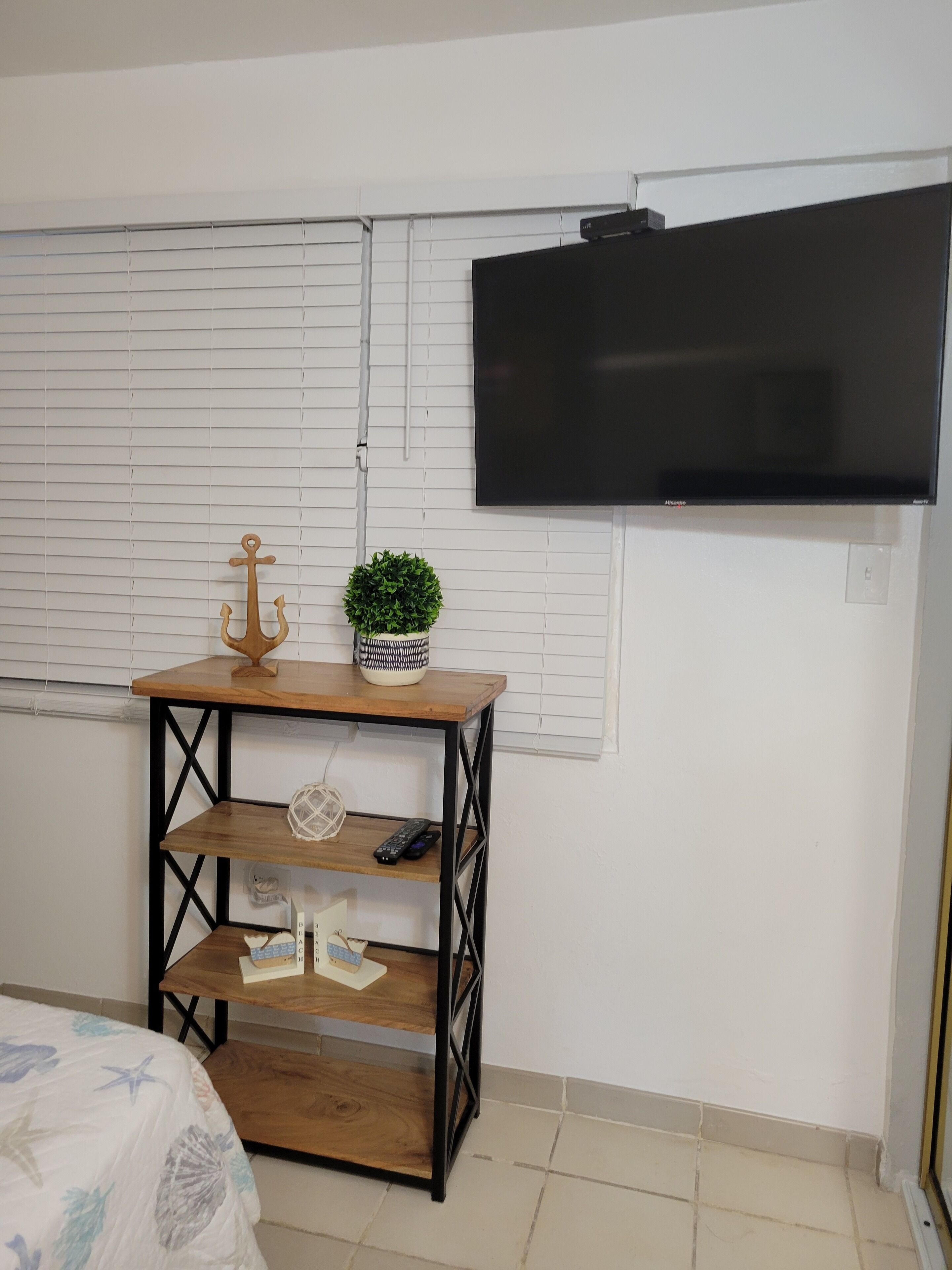 A bedroom with a bed, a wooden nightstand with a TV, and a window with blinds.