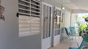 A room with a white wall, a window with blinds, a door, and a seating area with chairs and a table. - Playa icacos (Fajardo)