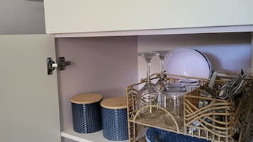 A kitchen with a microwave, two blue patterned containers, a wicker basket with glassware, a white towel, and a blue bottle.