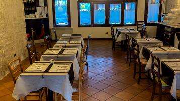 Un restaurante con varias mesas, sillas y un candelabro. Hay ventanas con vistas al exterior.
