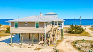 A wooden beach house with a balcony and a small tower, situated on a sandy beach with a clear view of the ocean. - 5 Bedroom Beach House Slps 12 - Private Beach - Shells - Fishing -Screened porch (Panacea)