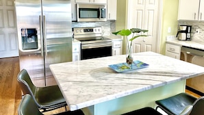 A kitchen with white cabinets, stainless steel appliances, a marble countertop, and a water dispenser. - 5 Bedroom Beach House Slps 12 - Private Beach - Shells - Fishing -Screened porch (Panacea)