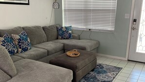 A living room with a grey sectional sofa, a brown ottoman, and a patterned rug.